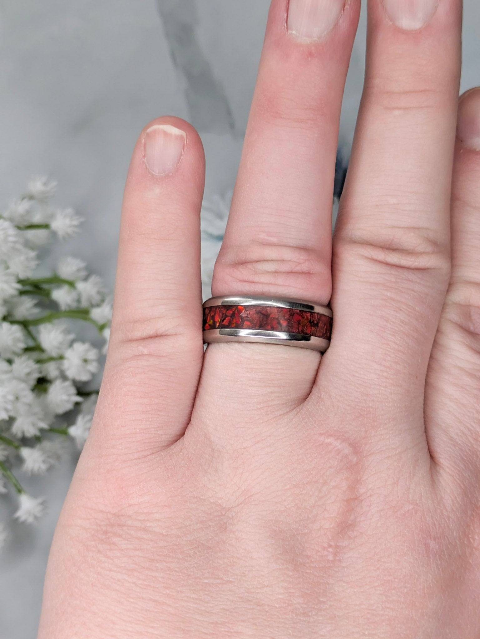 Vibrant red fire opal in a stainless steel inlay channel ring. The ring is on a finger with white flowers in the background.