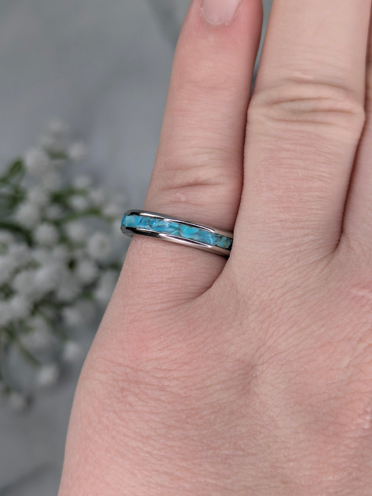 Raw natural blue Kingman turquoise in a stainless steel inlay ring channel. The ring is on a pinky finger with white flowers in the background.