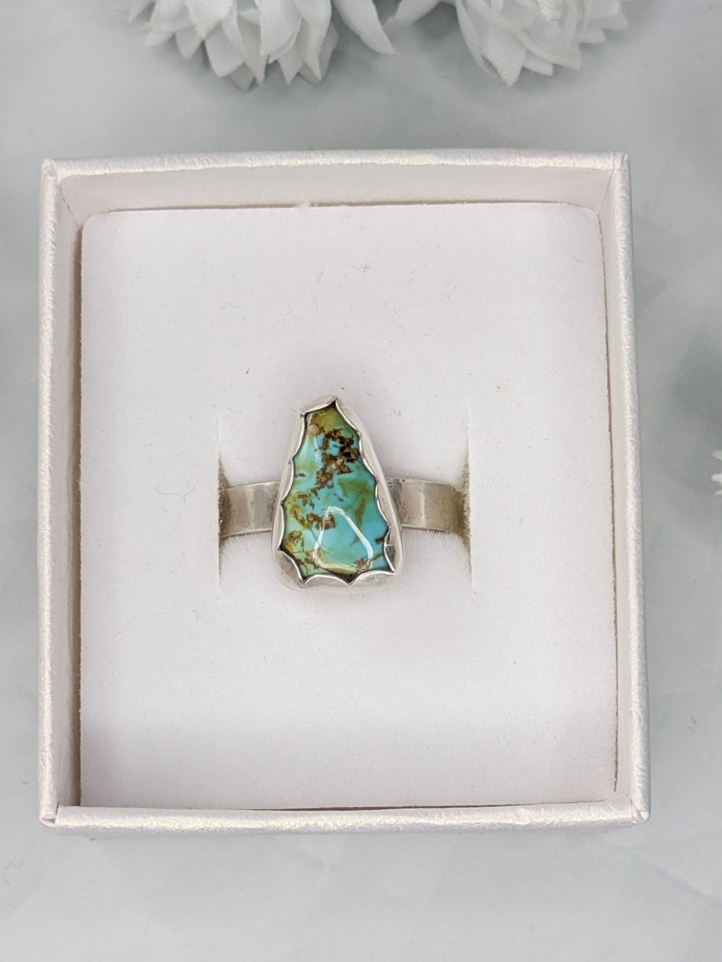 Sterling silver ring with a triangular turquoise gemstone. The turquoise is a rich sky blue and leaf green with specks of brown. The ring is in a white jewelry box.