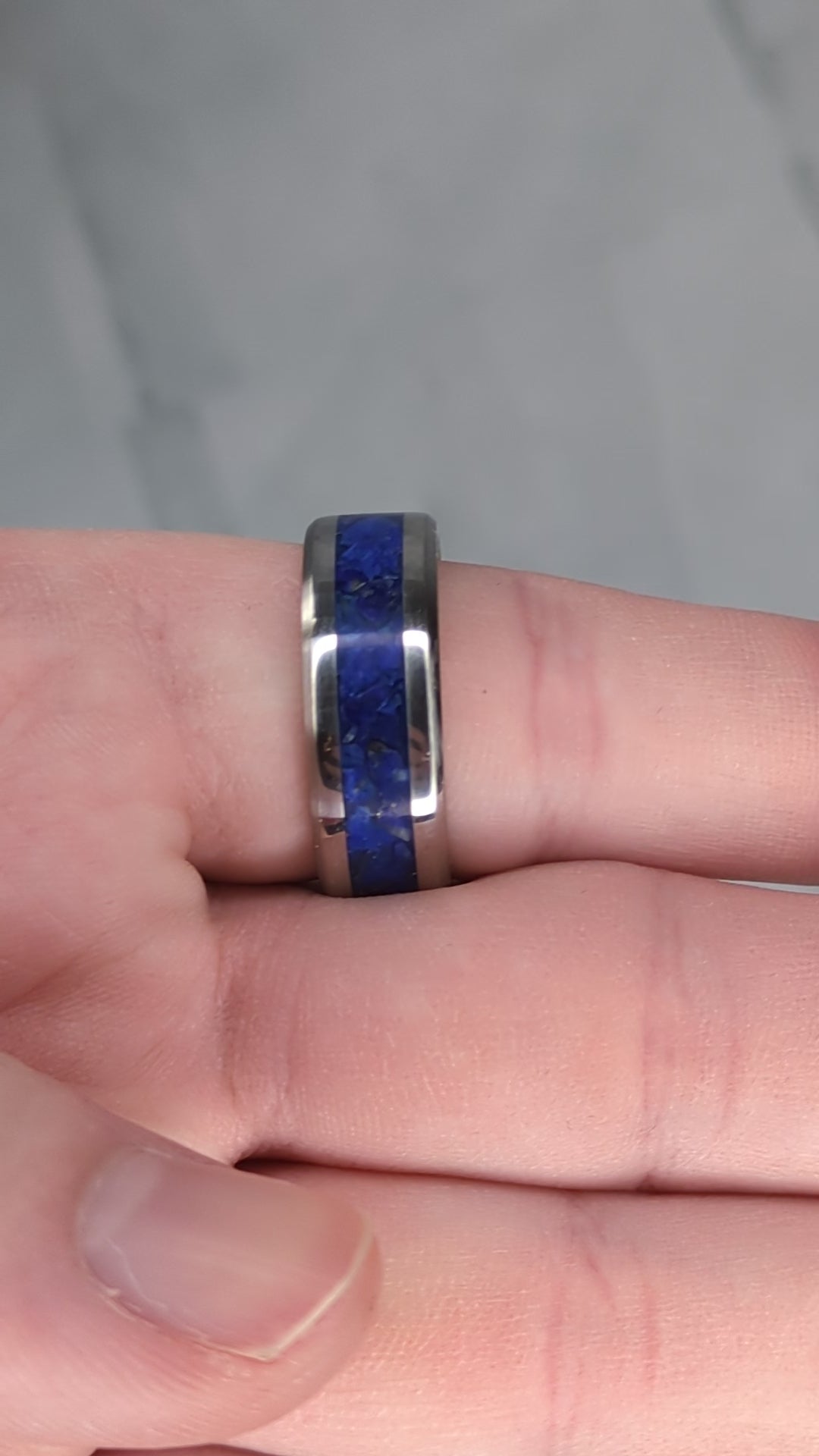 Blue lapis lazuli with flakes of gold pyrite in a stainless steel ring inlay channel. The ring is on a finger and rotated in the video to show off the vibrant color and shine.
