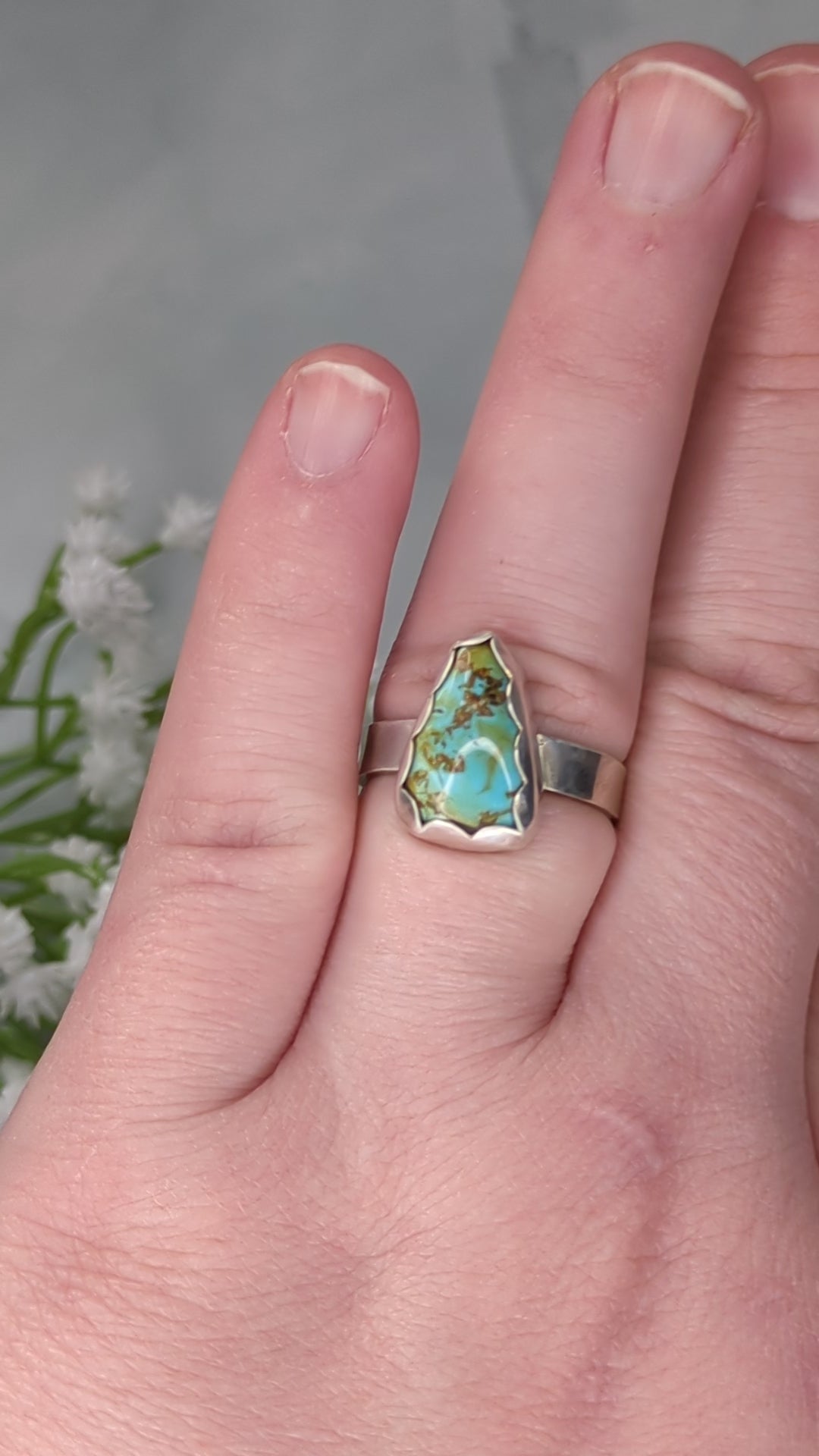 Sterling silver ring with a triangular turquoise gemstone. The turquoise is a rich sky blue and leaf green with specks of brown. The ring is on a finger and rotated to show the shine of the silver and turquoise.