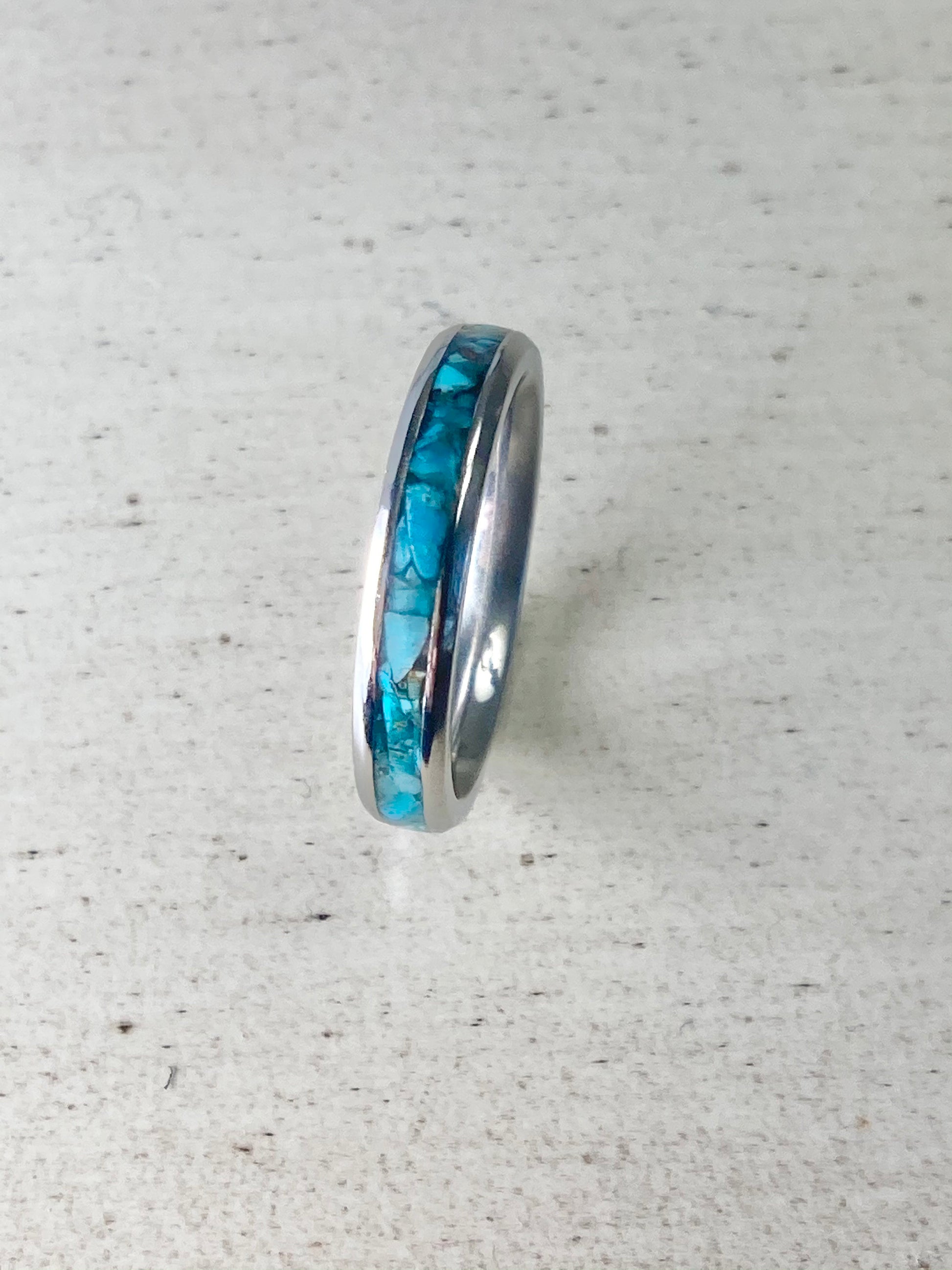 Raw natural blue Kingman turquoise in a stainless steel inlay ring channel. The ring is in on a wood table.