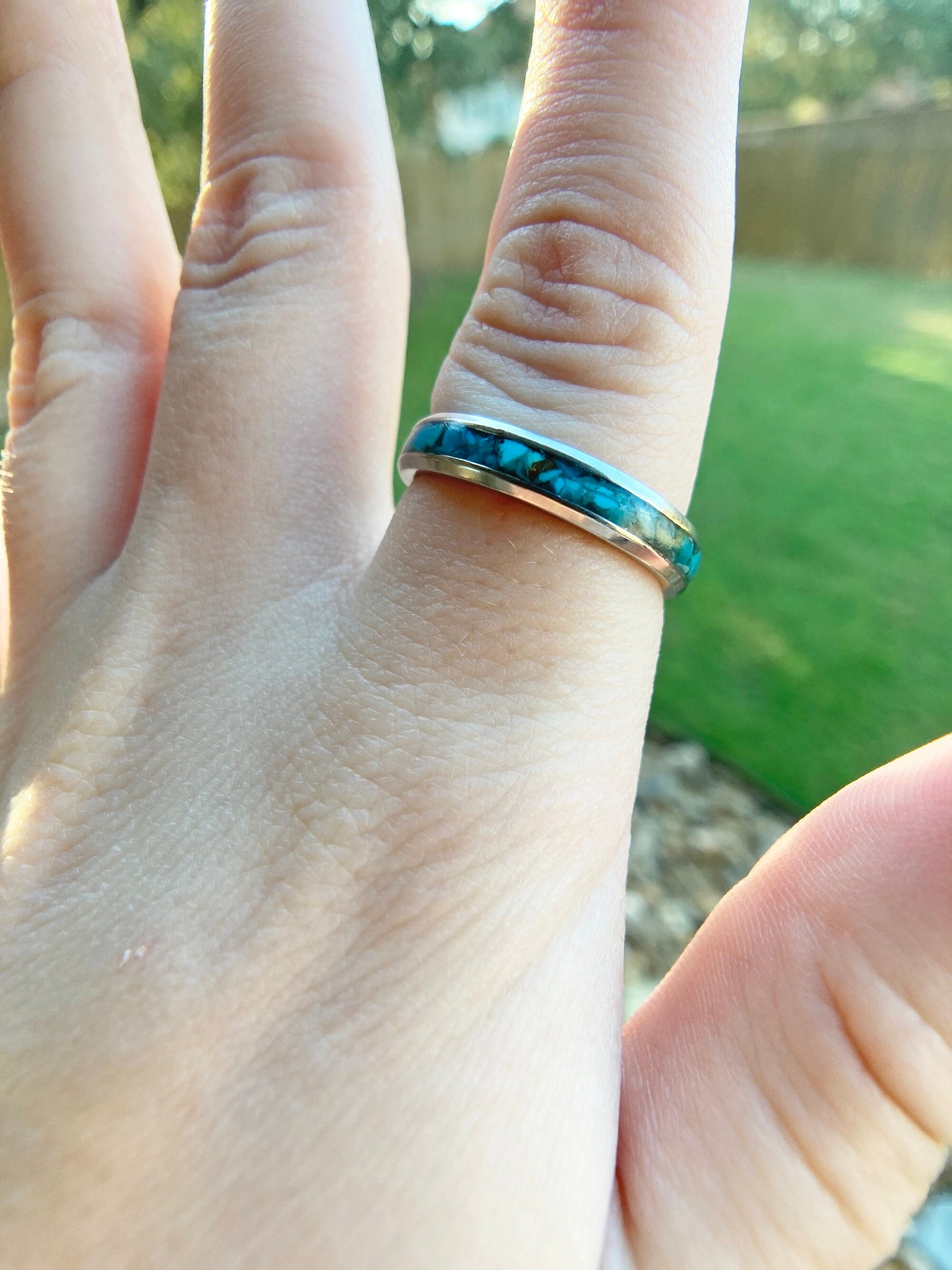 Raw natural blue Kingman turquoise in a stainless steel inlay ring channel. The ring is on a finger with green grass in the background.