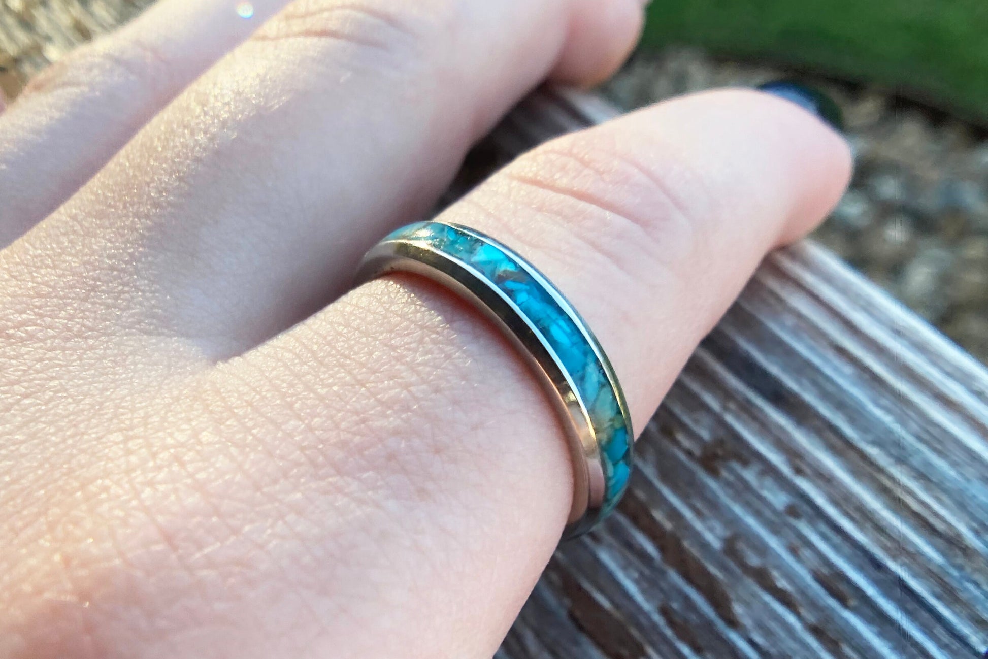 Raw natural blue Kingman turquoise in a stainless steel inlay ring channel. The ring is on a finger with wood and grass in the background.