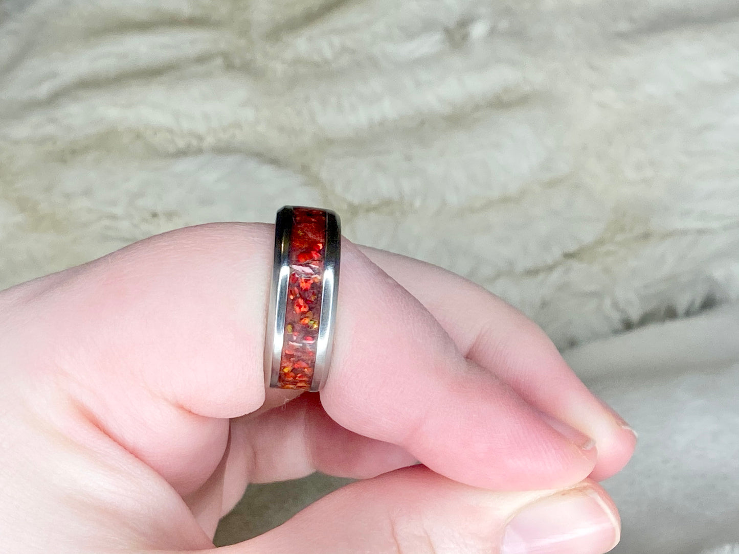 Vibrant red fire opal in a stainless steel inlay channel ring. The ring is on a finger with a white blanket in the background.