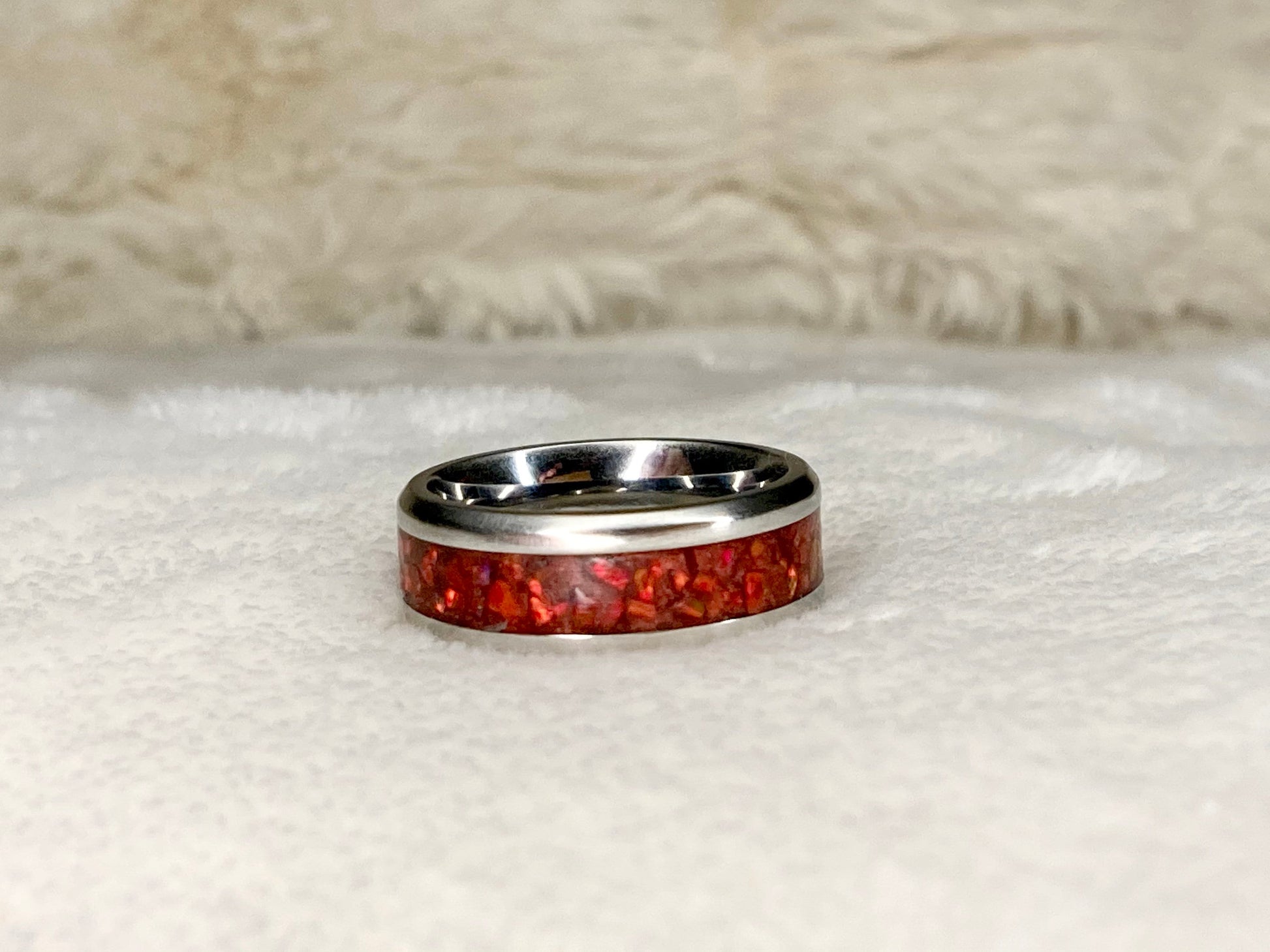 Vibrant red fire opal in a stainless steel inlay channel ring. The ring is on a white blanket.