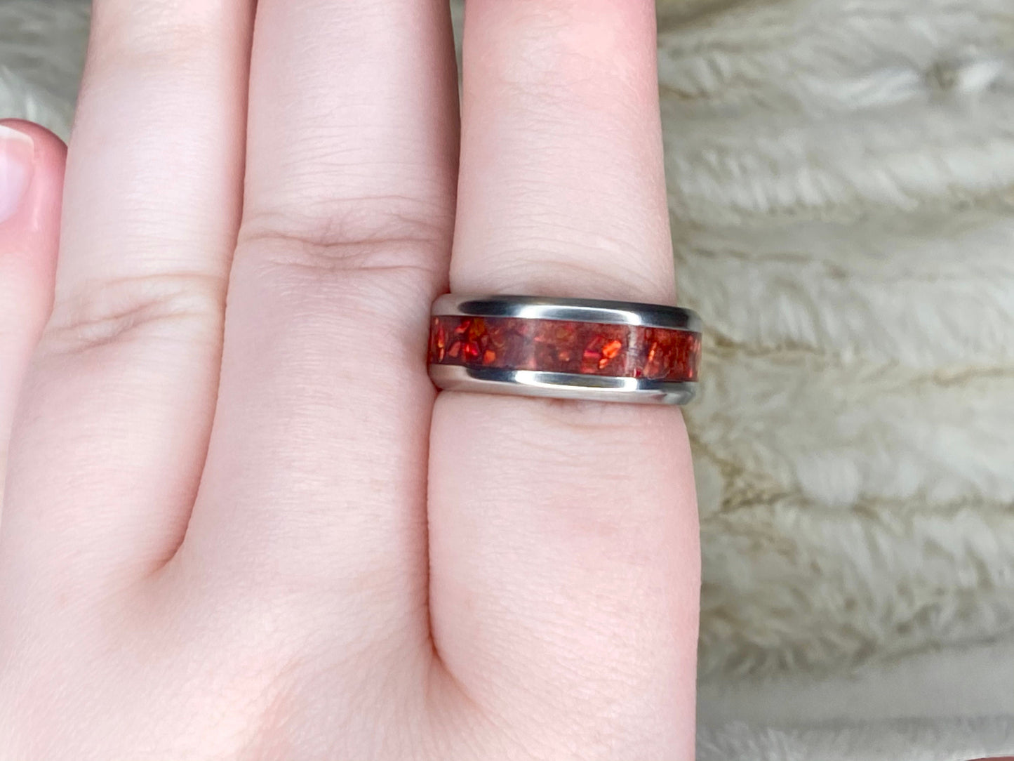 Vibrant red fire opal in a stainless steel inlay channel ring. The ring is on a finger with a white blanket in the background.