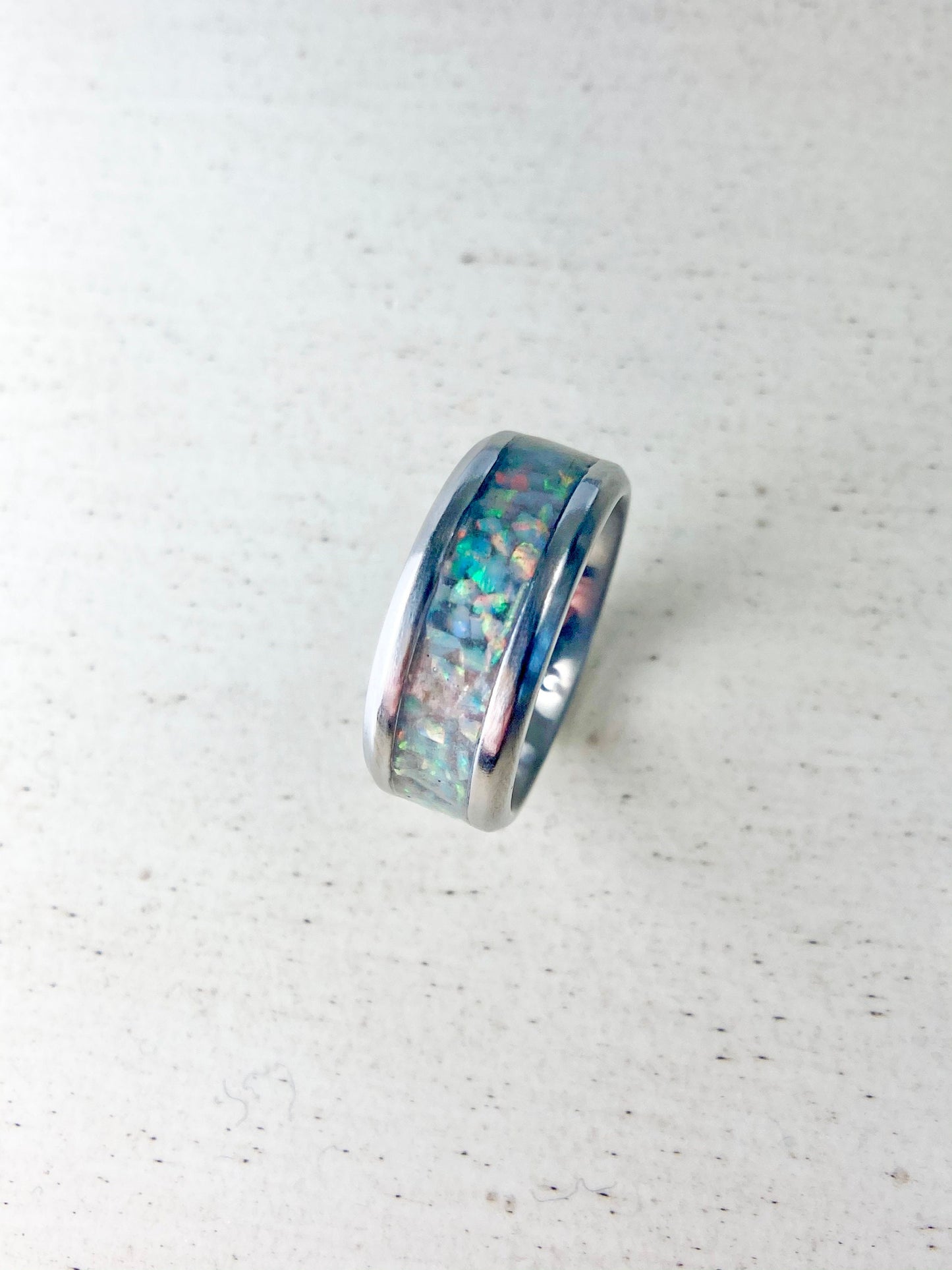 Rainbow-hued white fire and ice opal in a stainless steel inlay channel ring. The light shows off vibrant pink, green, orange, yellow, and red hues. The ring is on a wood table.