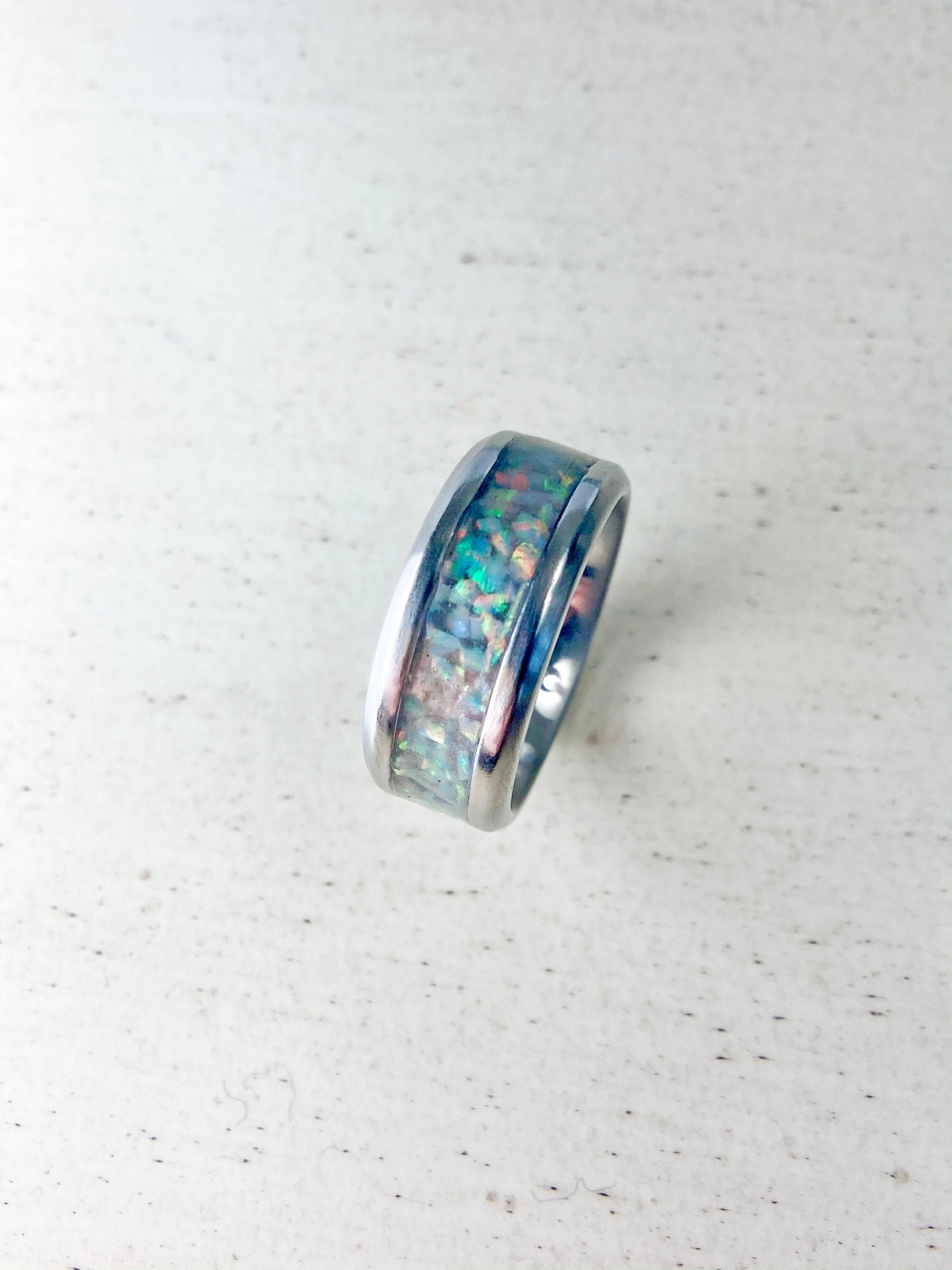 Rainbow-hued white fire and ice opal in a stainless steel inlay channel ring. The light shows off vibrant pink, green, orange, yellow, and red hues. The ring is on a wood table.